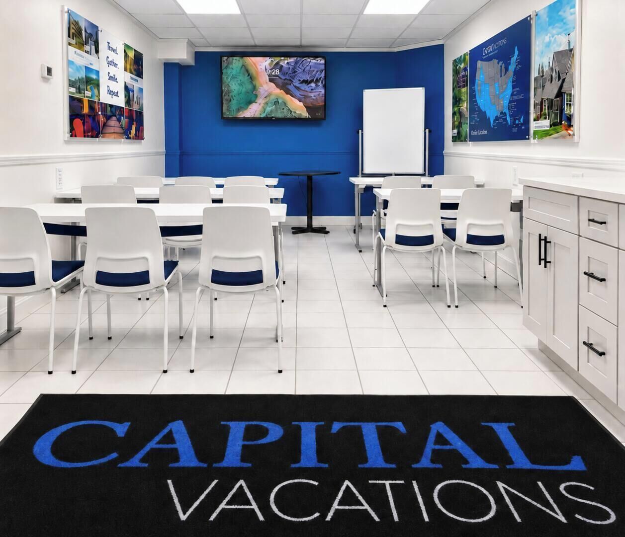 Une salle de conférence avec des chaises blanches et un tapis noir orné du texte « CAPITAL VACATIONS ».