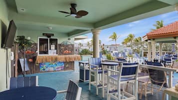 An outdoor seating area with tables and chairs, a poolside bar, and a ceiling fan.