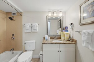 A bathroom with a shower, toilet, sink, and a framed picture on the wall.