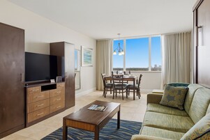 Una sala de estar moderna con un televisor de pantalla plana, armarios de madera, una mesa de comedor con sillas, un sofá y un ventanal con vista a la ciudad.