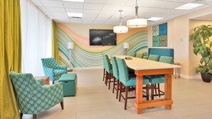 Een vergaderruimte met een lange tafel, stoelen, een televisie en een kleurrijk wanddecor.