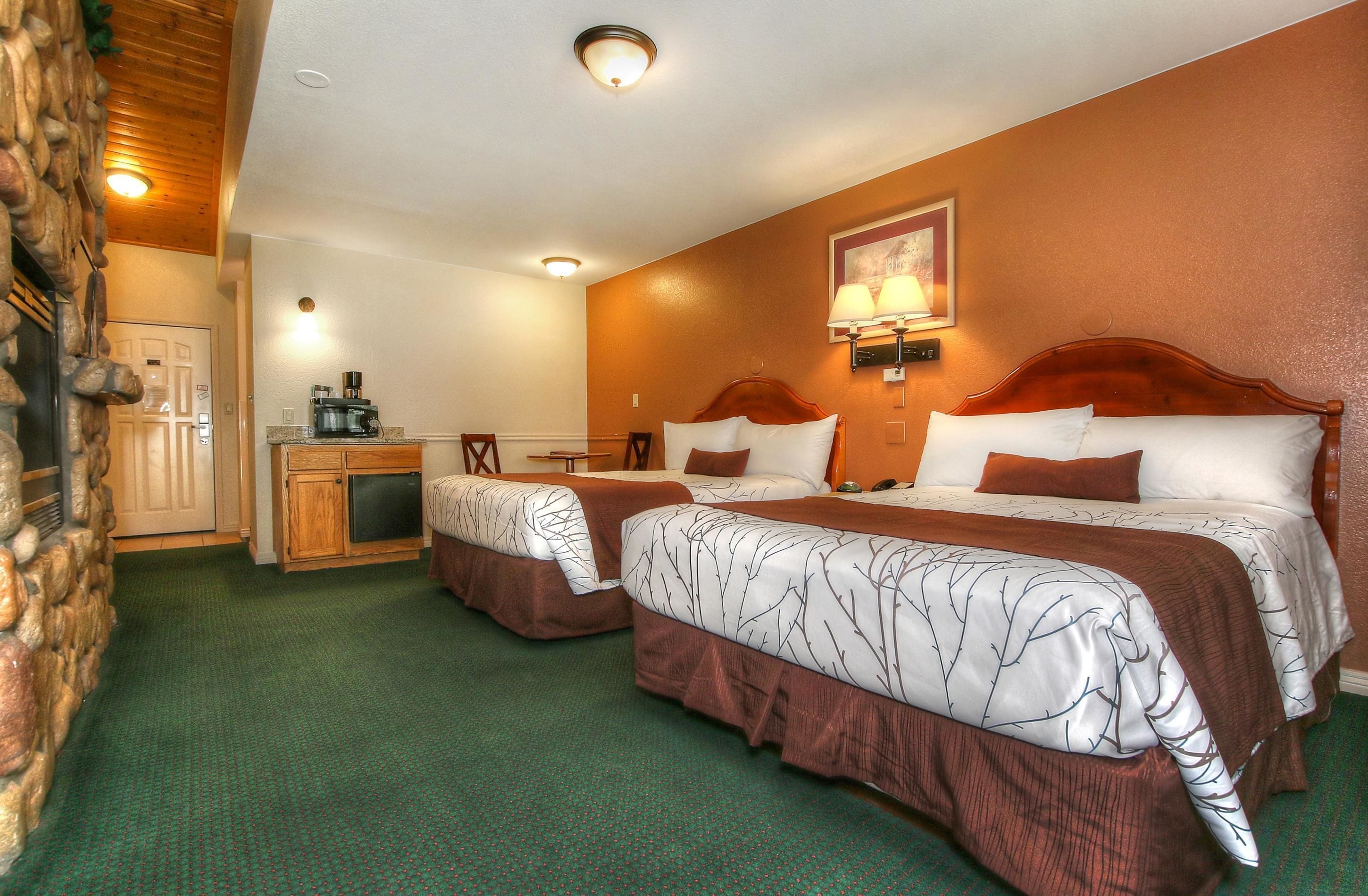 A hotel room with two beds, a desk, a coffee machine, and a stone wall.