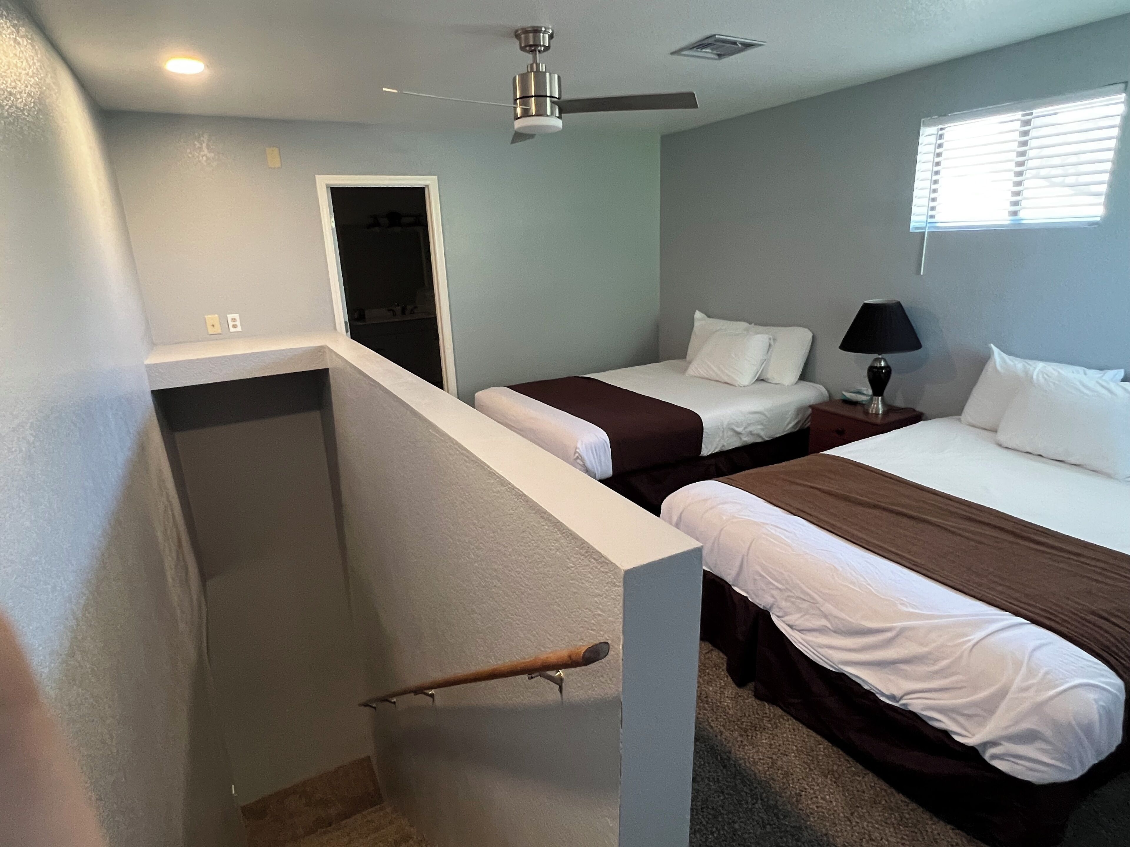 Quarto com duas camas, um ventilador de teto, uma janela com persianas e uma porta que dá para um armário.