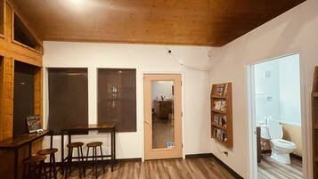 A spacious room with a wooden floor, a ceiling fan, a dining area with stools, and a view into the bathroom.