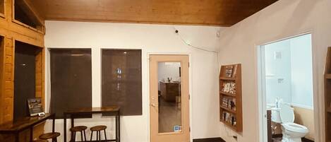 A spacious room with a wooden floor, a ceiling fan, a dining area with stools, and a view into the bathroom.