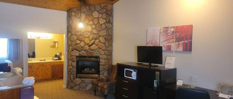 A hotel room with a stone fireplace, a television on a cabinet, a desk with a computer, and a chair.