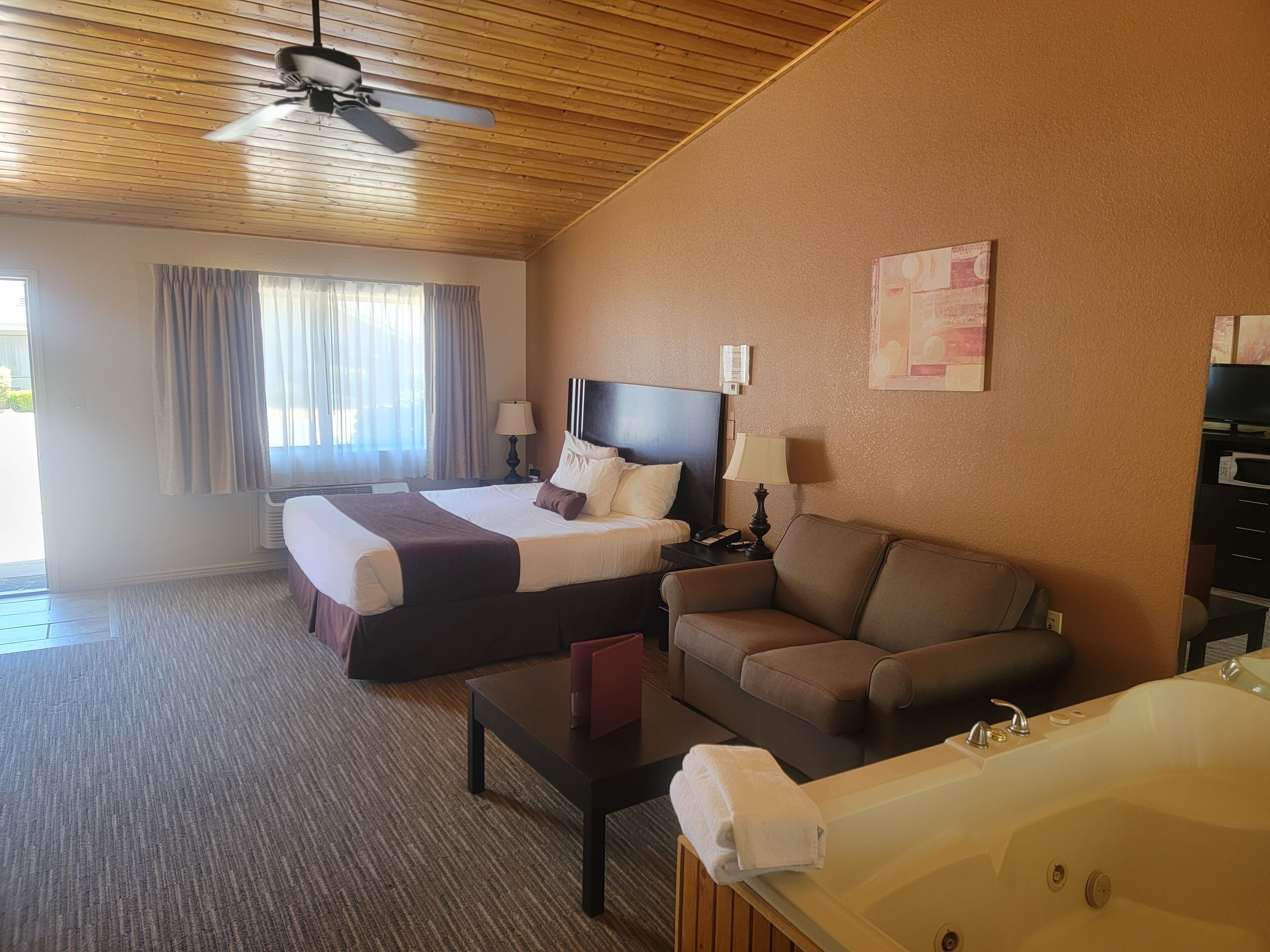 Une chambre d’hôtel équipée d’un lit, d’un canapé, d’un bureau, d’une lampe, d’un ventilateur de plafond et d’une baignoire.