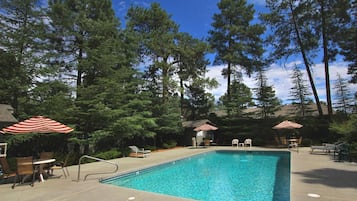A rectangular swimming pool with a metal ladder, surrounded by lounge chairs and red and white striped umbrellas.