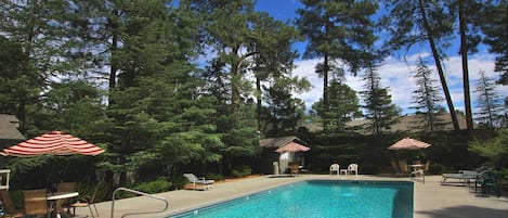 A rectangular swimming pool with a metal ladder, surrounded by lounge chairs and red and white striped umbrellas.