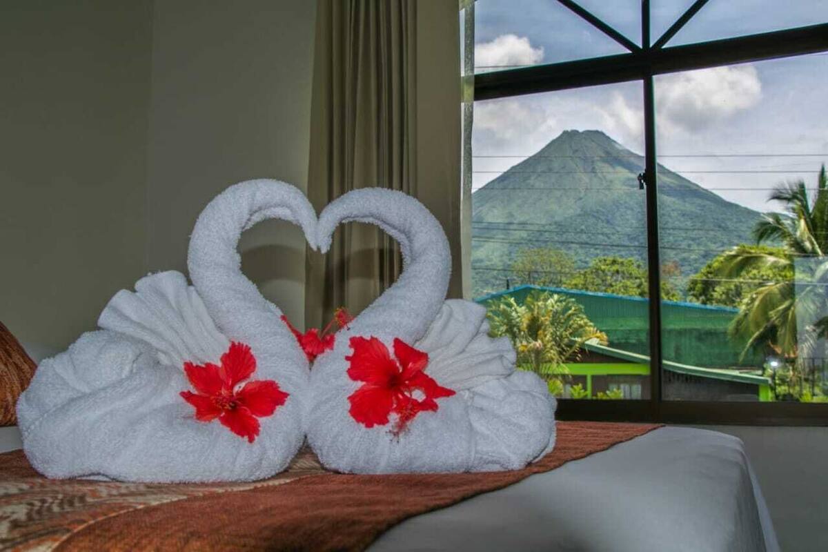 Ein Bett mit Blick auf einen Berg und Palmen durch ein Fenster.