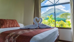 Une chambre d’hôtel avec un lit, une décoration en forme de cœur réalisée avec des serviettes, une vue sur une montagne et une fenêtre avec des rideaux.