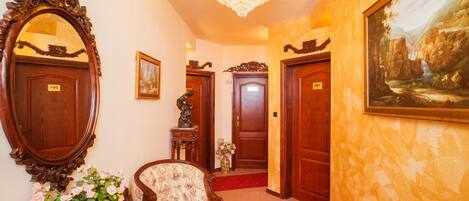 A hallway with ornate wooden doors, a large mirror, a chandelier, and a red carpet.