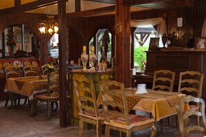 A dining area with wooden tables and chairs, a chandelier, and various decorative items. - Dallas Residence (Varna)