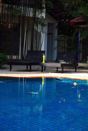 A pool area with two black lounge chairs and a yellow bottle on the edge. - Orient D'angkor (Siem Reap)