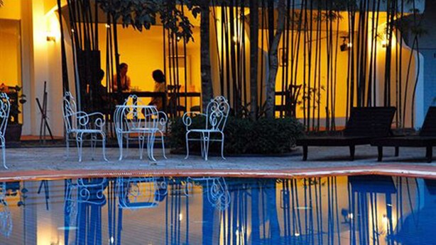 A poolside area with metal chairs and a bench, surrounded by bamboo plants. - Orient D'angkor (Siem Reap)