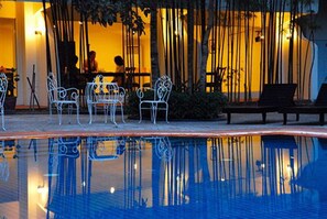Un espace aménagé au bord de la piscine, avec des chaises et un banc en métal, entouré de plantes de bambou.