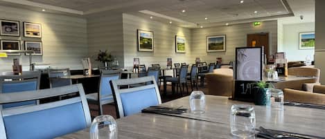 A hotel dining area with tables set for dining, chairs, and a menu stand.