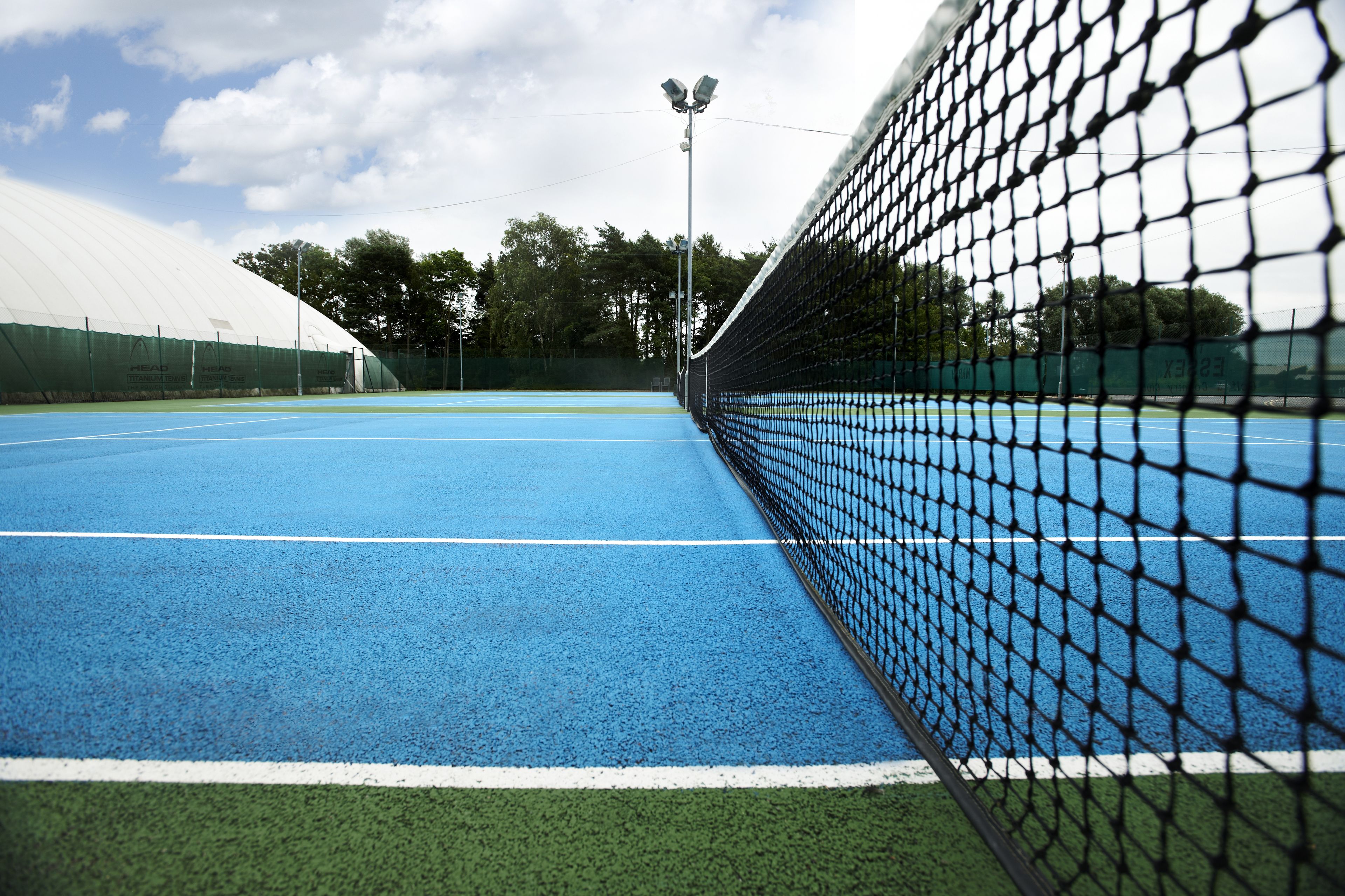 A tennis court with a net, blue surface, and green surrounding area.