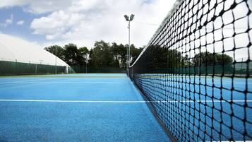 A tennis court with a net, blue surface, and green surrounding area.