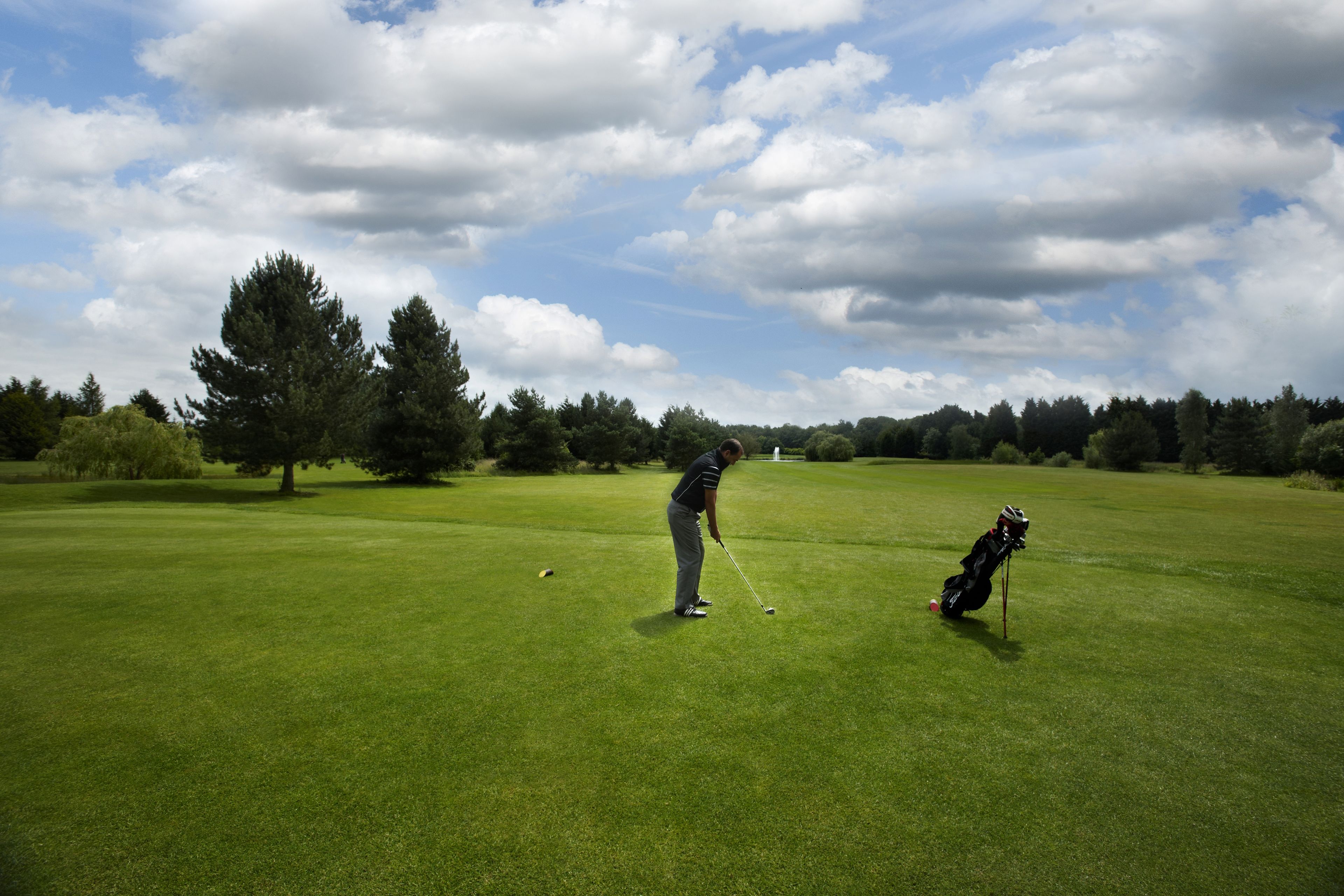 A golf course with a golfer preparing to putt, a golf bag, and a clear sky.