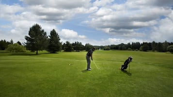 A golf course with a golfer preparing to putt, a golf bag, and a clear sky.