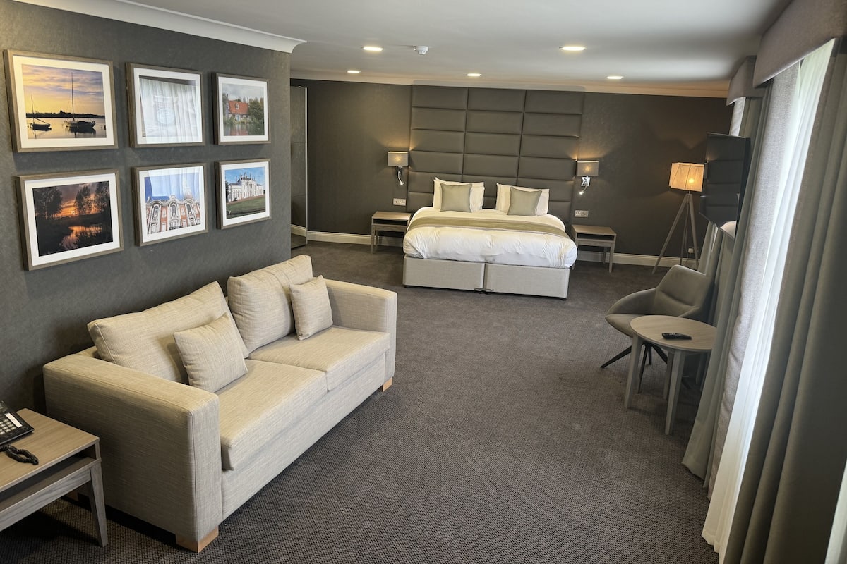 Une chambre d’hôtel avec un grand lit, un canapé, un bureau avec un téléphone et des tableaux encadrés au mur.