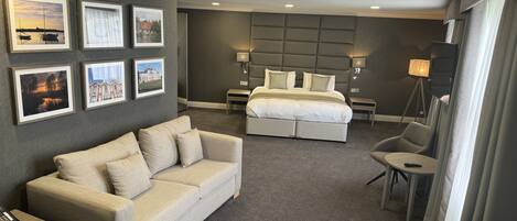 A hotel room with a large bed, a sofa, a desk with a phone, and framed pictures on the wall.