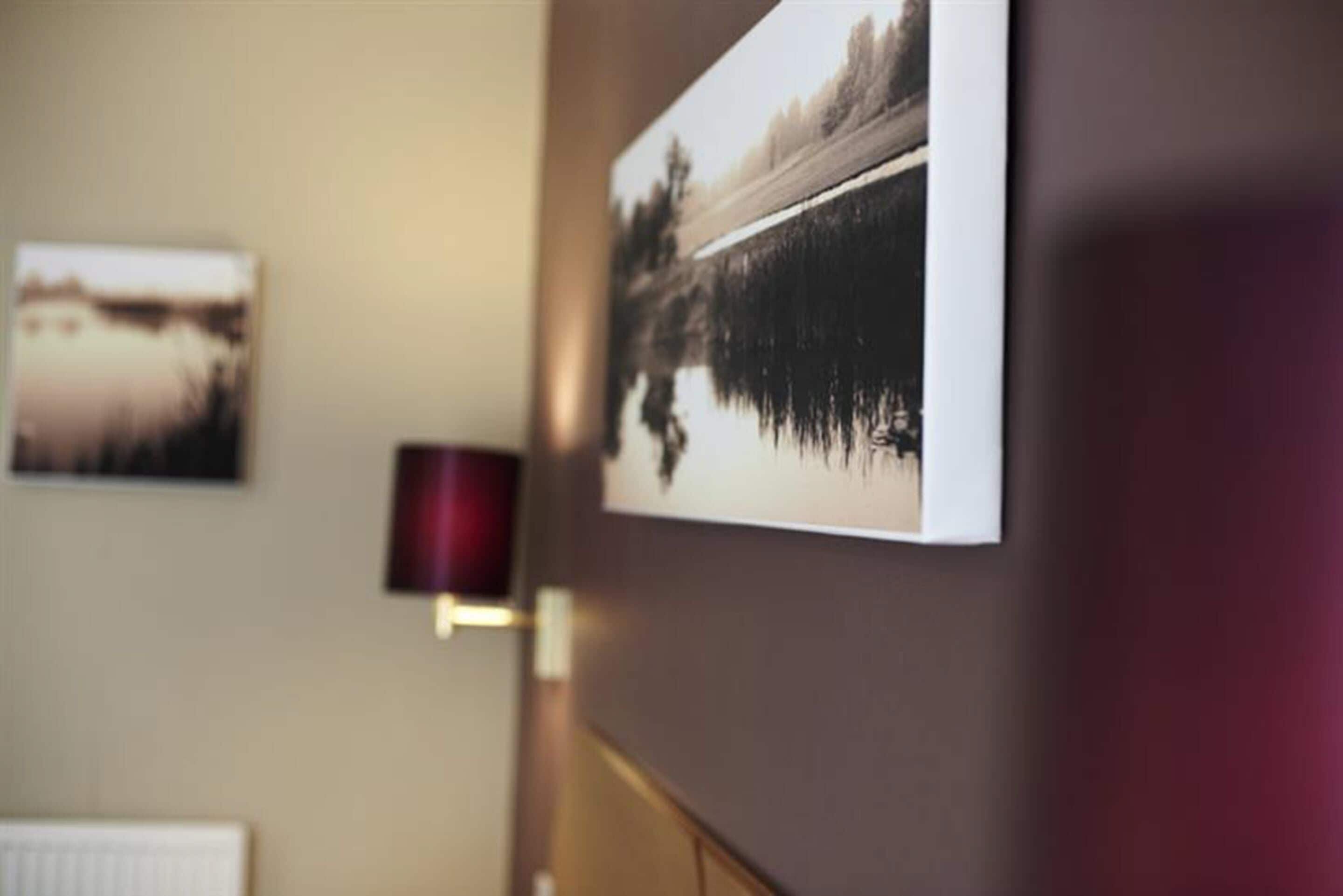 Un couloir orné d’un tableau représentant un paysage, accroché au mur, et d’une lampe rouge.