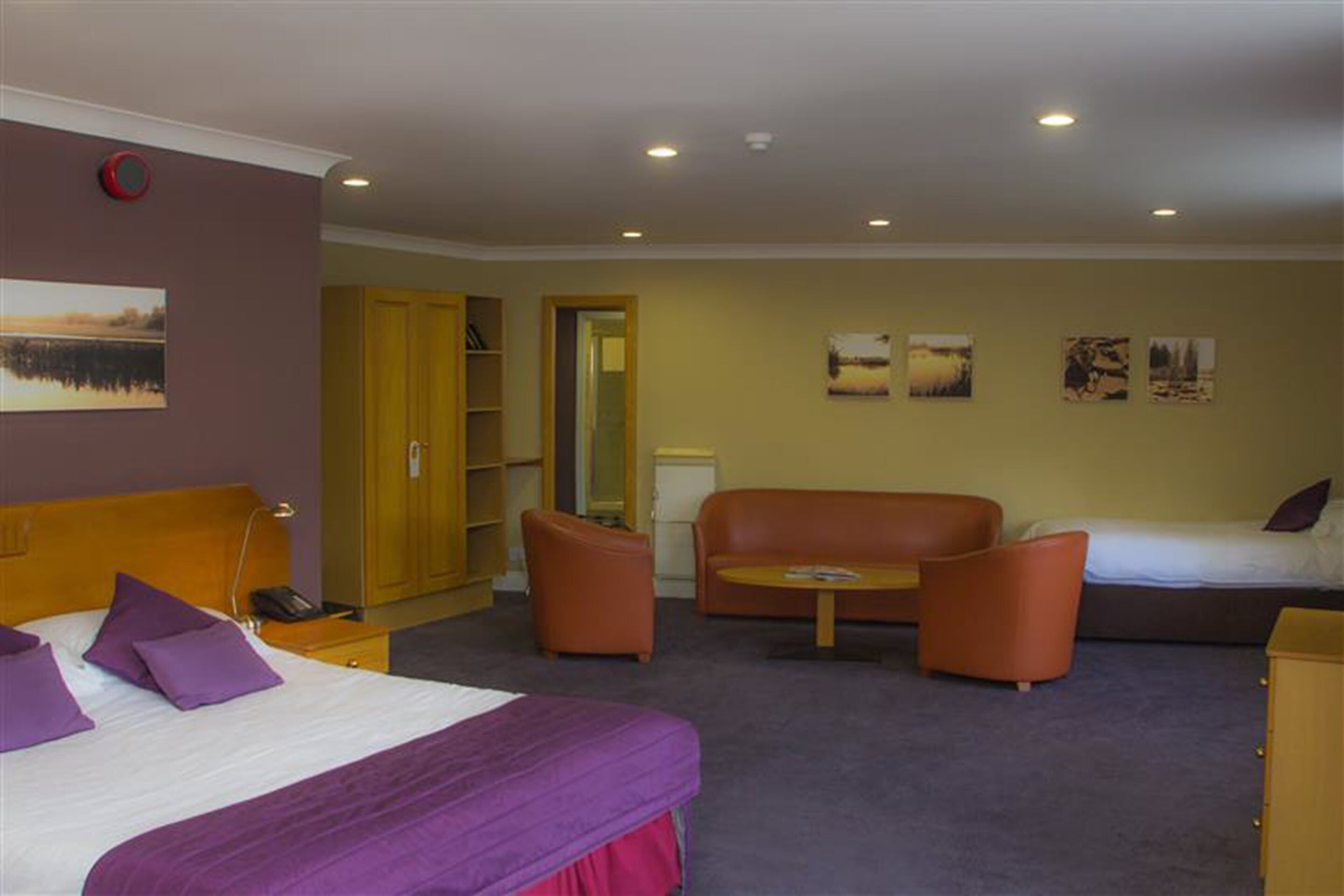 A hotel room with a bed, two armchairs, a sofa, a small table, and a wardrobe.