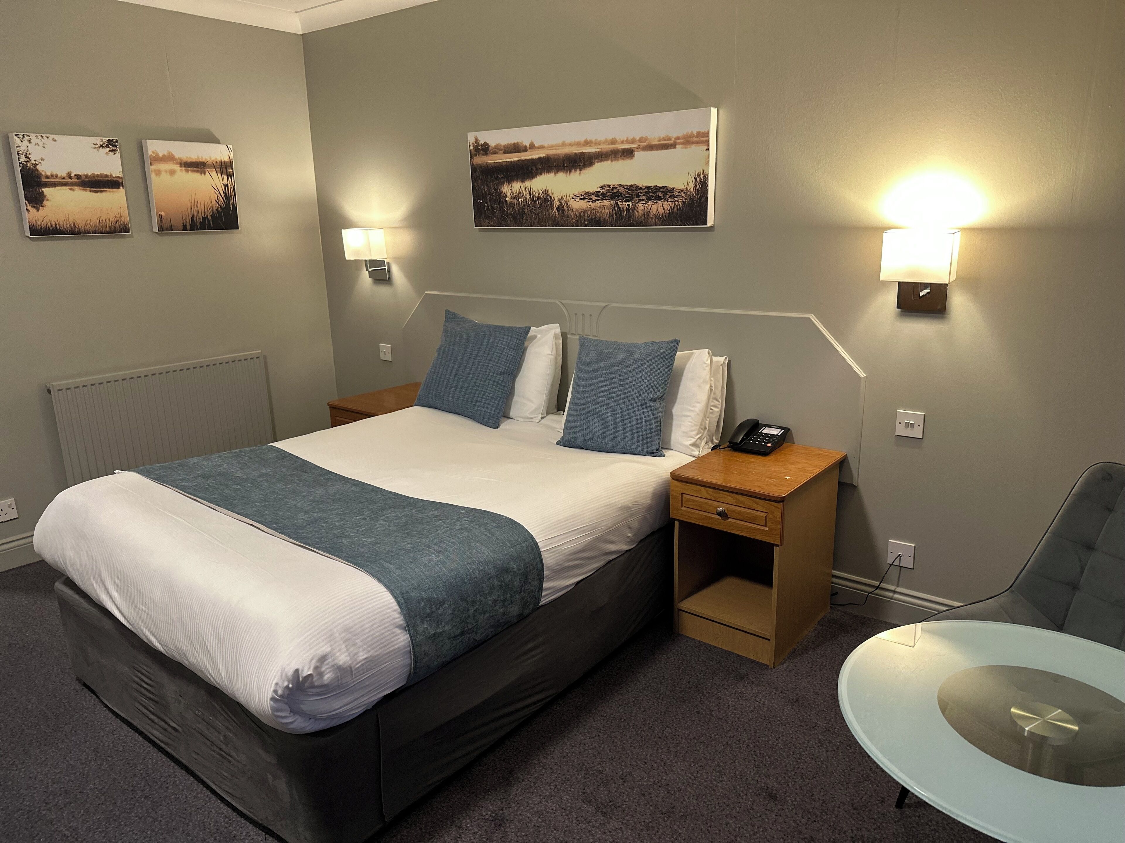 Una habitación de hotel con una cama grande, dos mesitas de noche, una silla y lámparas fijadas a la pared.