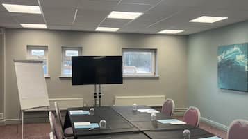 A conference room with a long table, chairs, a whiteboard, a large screen, and windows.