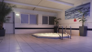 Ein Wellnessbereich mit Whirlpool, gefliestem Boden, Fenstern und Zimmerpflanzen.
