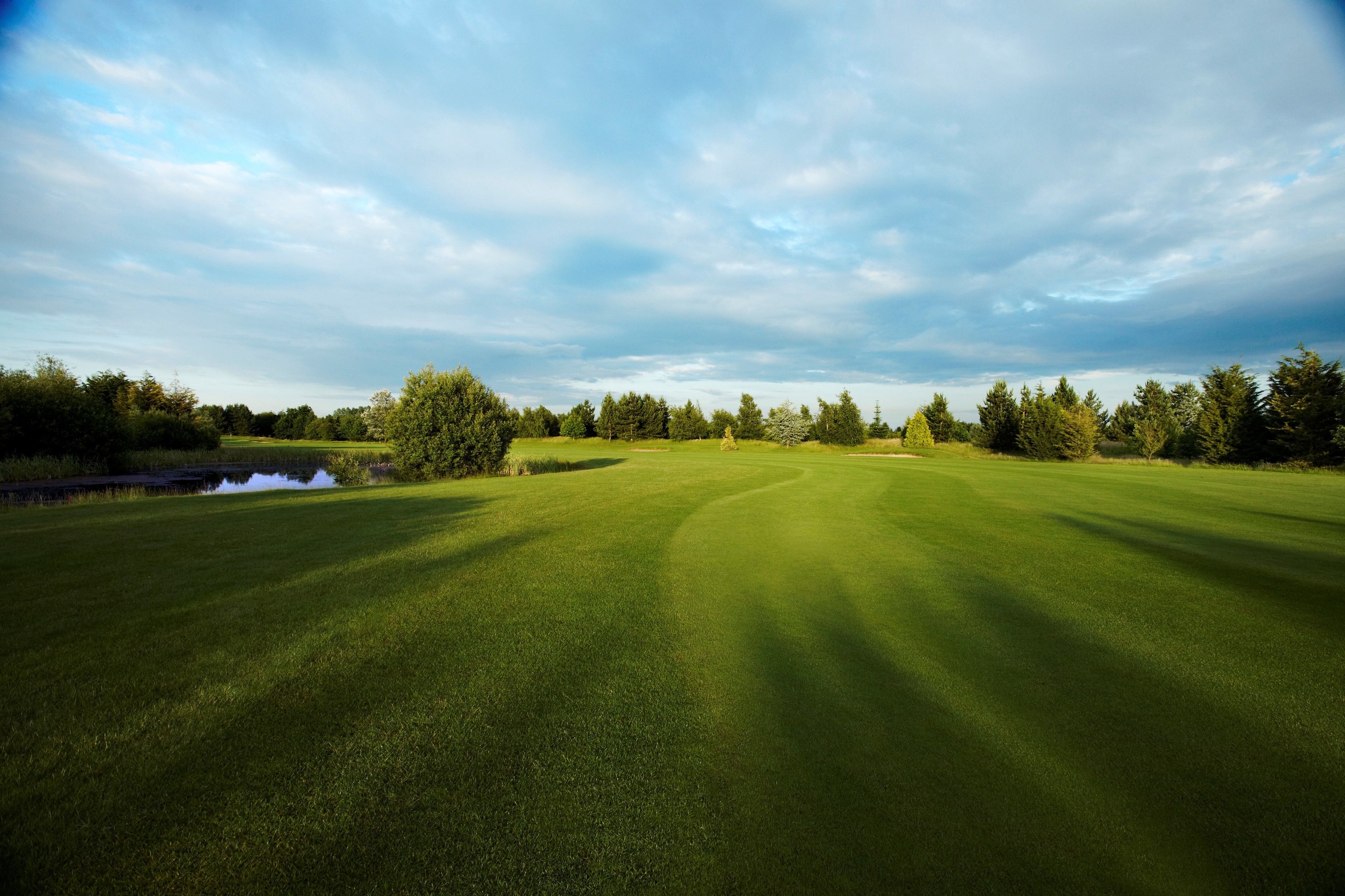 A golf course with a pond, trees, and a cloudy sky.