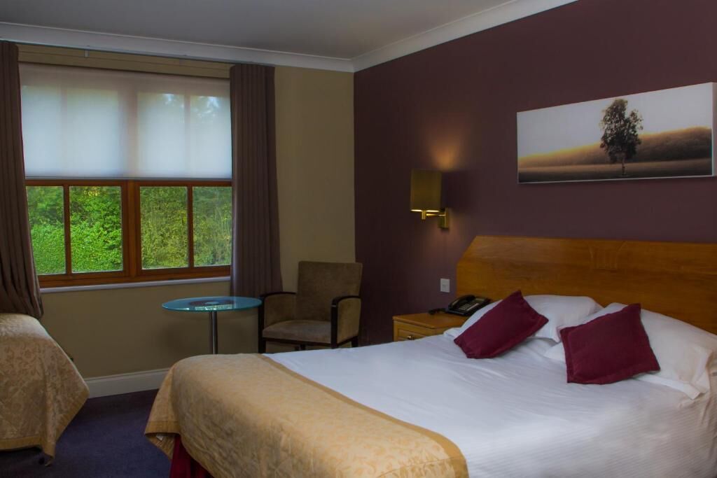 A hotel room with a large bed, two chairs, a small table, and a window with curtains.