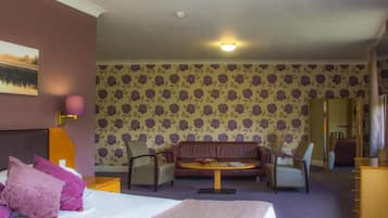 Habitación de hotel con cama, sofá, dos sillones, una mesita y una pared con papel tapiz floral.