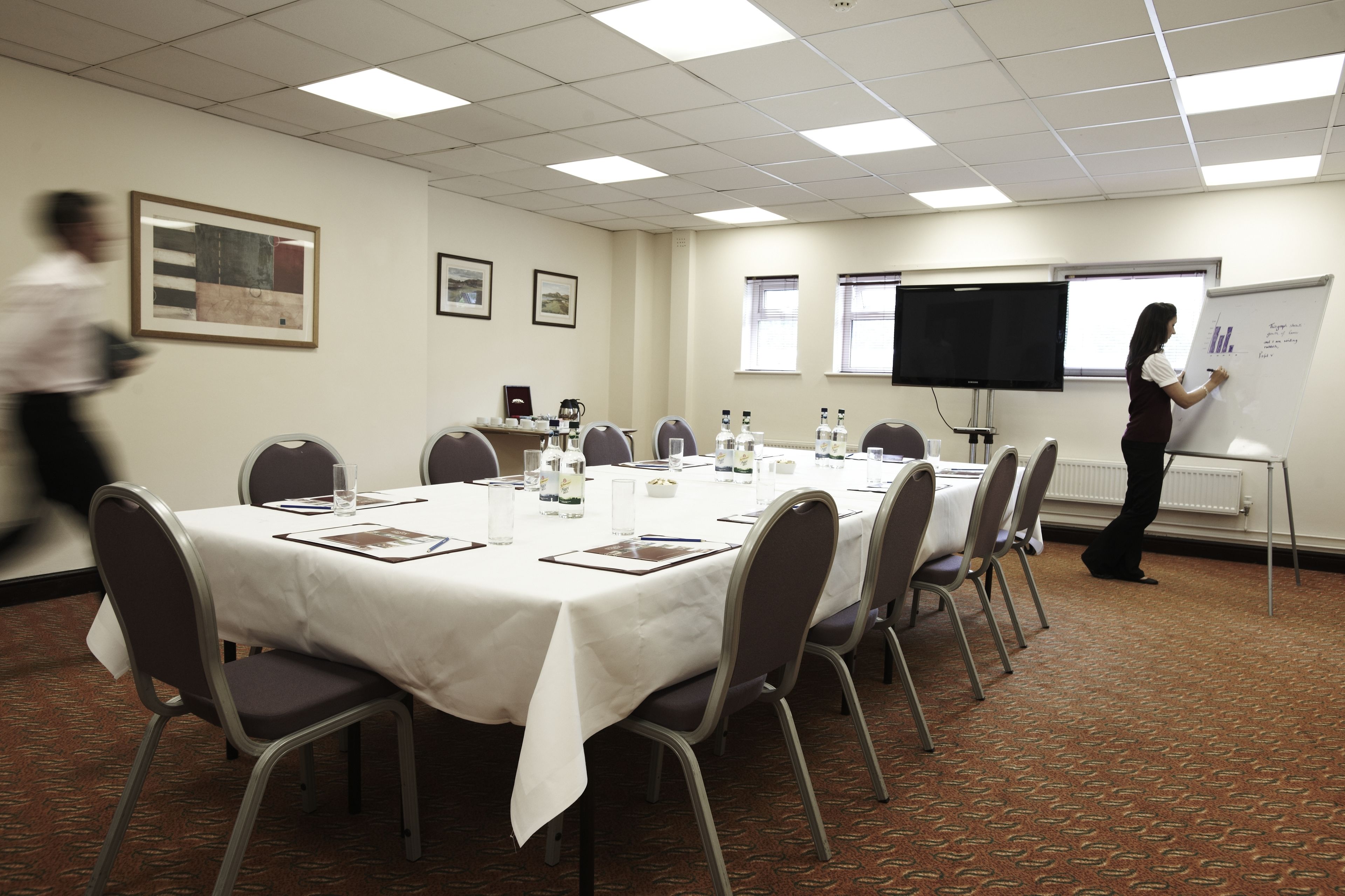 A conference room with a white table, chairs, a whiteboard, and a projector screen.