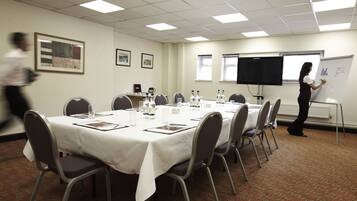 A conference room with a white table, chairs, a whiteboard, and a projector screen.
