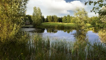 Een vredig landschap met een vijver, weelderige begroeiing en een golfbaan in de verte.