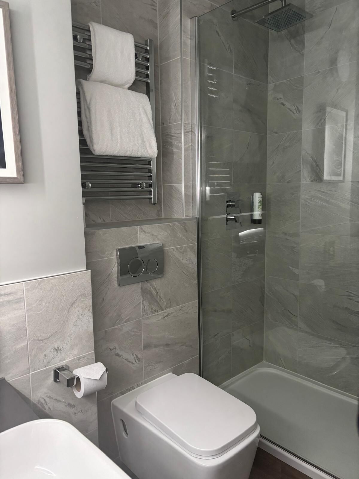 A modern bathroom with a glass-enclosed shower, a toilet, and a towel rack with two towels.