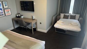 Une chambre d’hôtel avec un lit, un bureau, une chaise, une télévision et une fenêtre avec des rideaux.