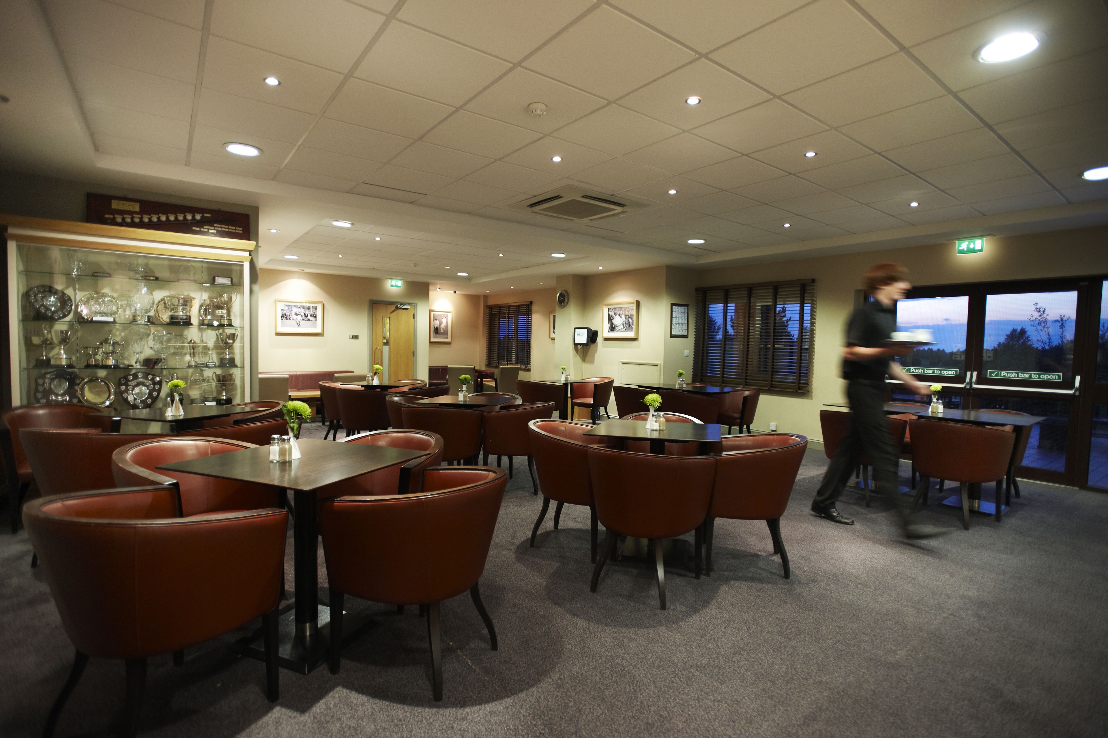 A dining area with multiple tables and chairs, a display case with glassware, and a view through the windows.