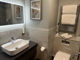 Un baño moderno con un lavamanos grande, un espejo, un perchero para toallas y un inodoro.