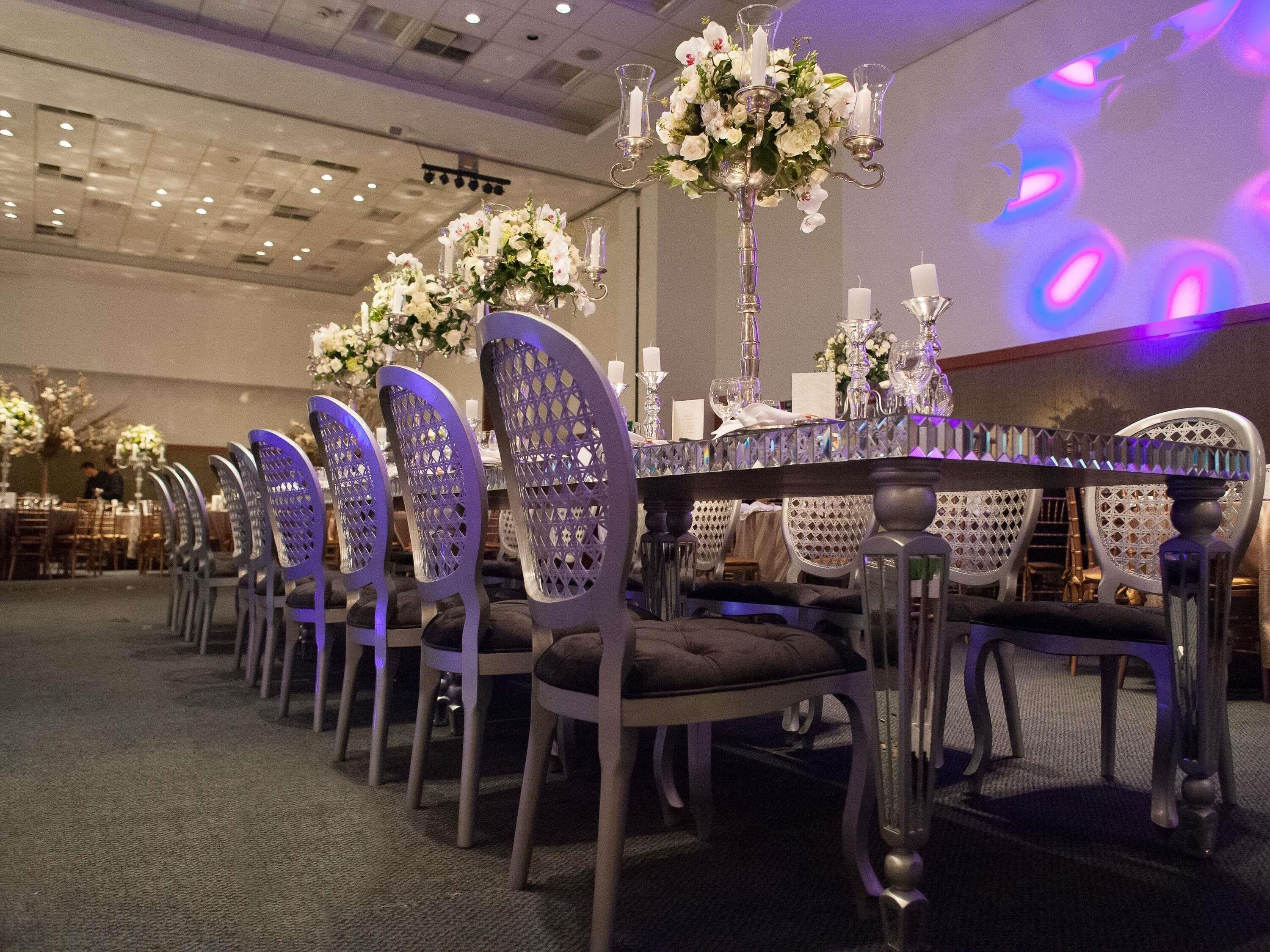 A banquet hall with a long table, chairs, and floral centerpieces.