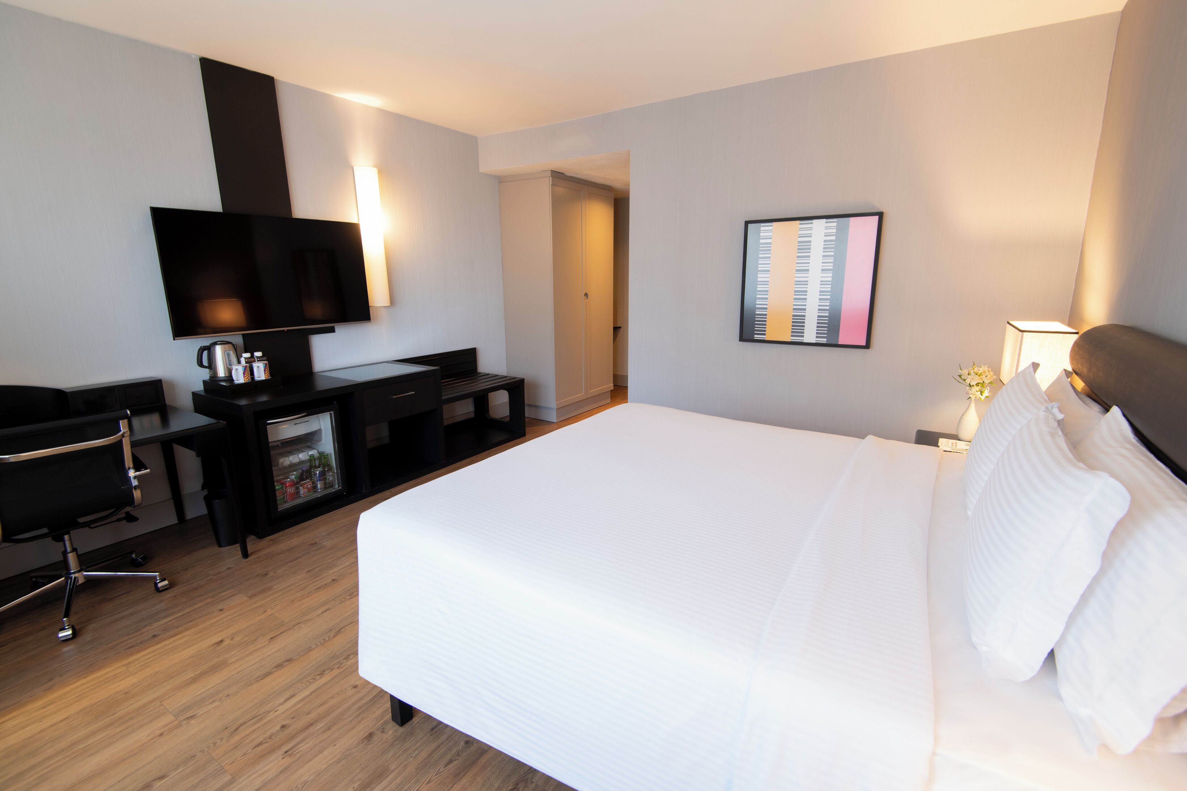 A hotel room with a bed, a desk with a chair, a television, and a wall-mounted picture.