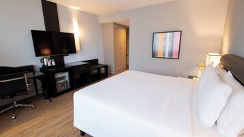 A hotel room with a bed, a desk with a chair, a television, and a wall-mounted picture.