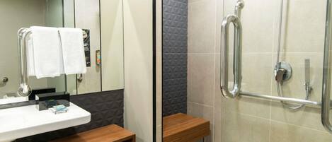 A modern bathroom with a glass shower enclosure, a wooden bench, a sink with a mirror, and a towel rack.