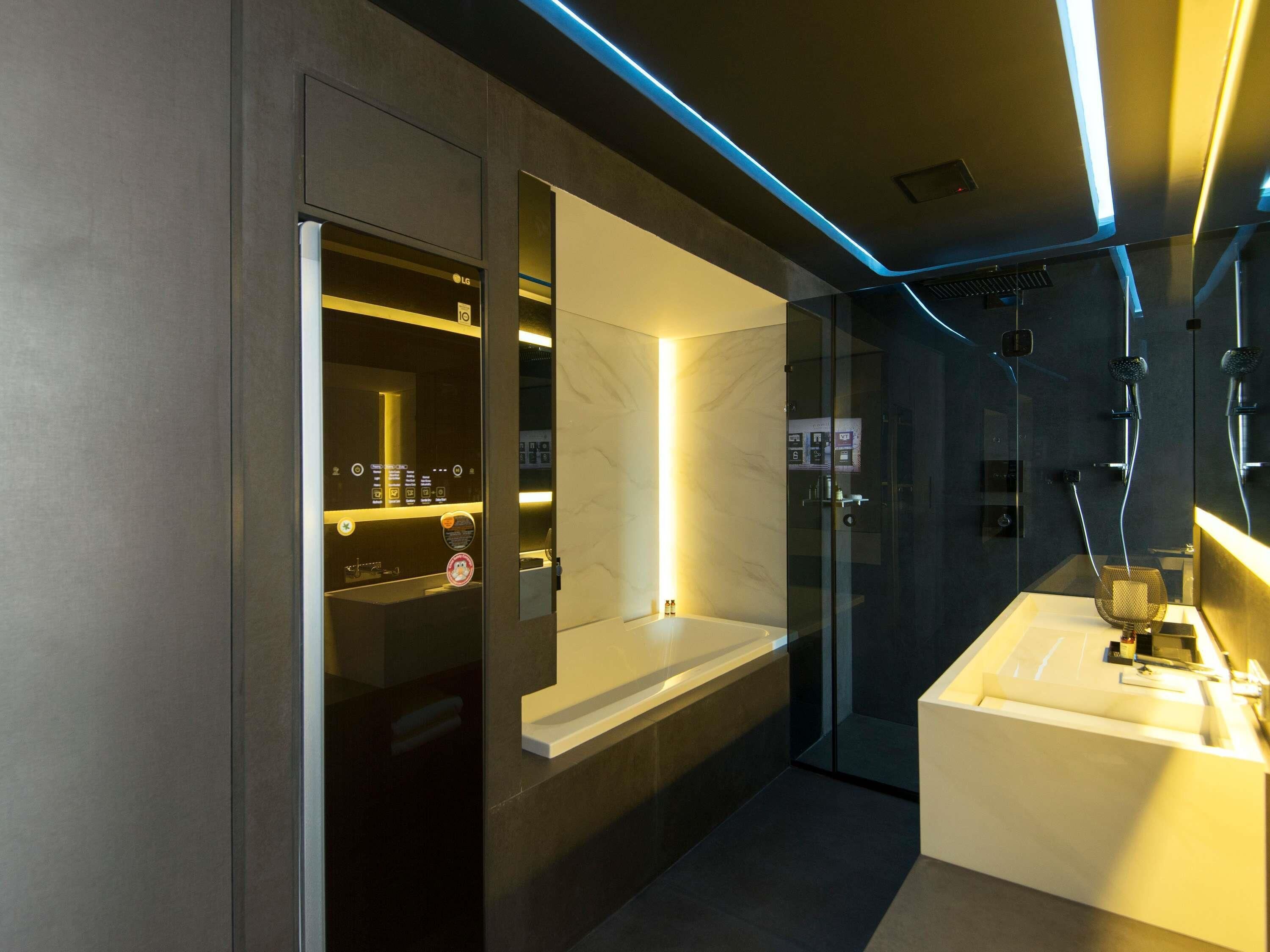 Un baño moderno con mampara de vidrio, tocador con espejo y refrigerador LG empotrado.