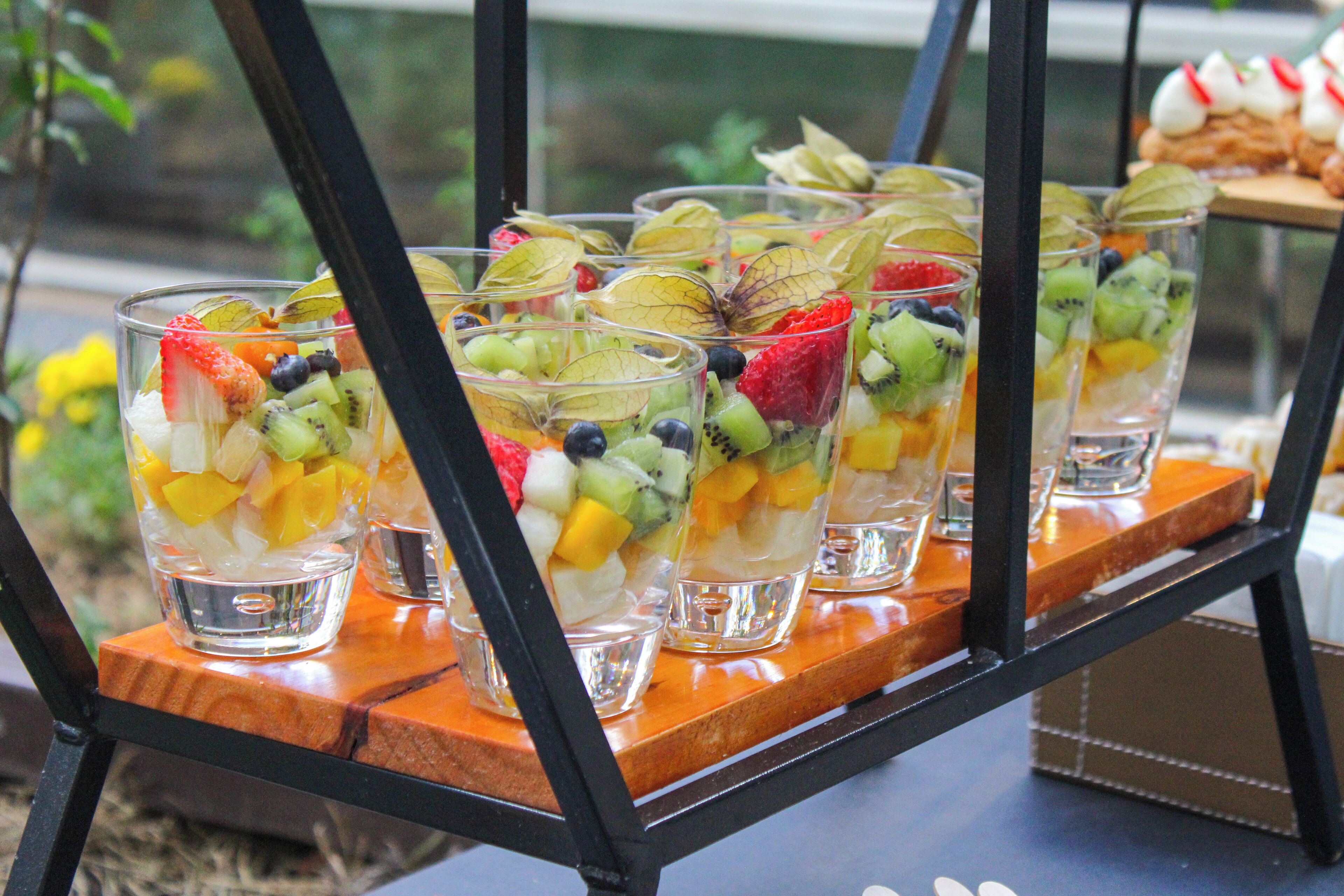 A display of fruit parfaits in clear glasses on a wooden shelf.