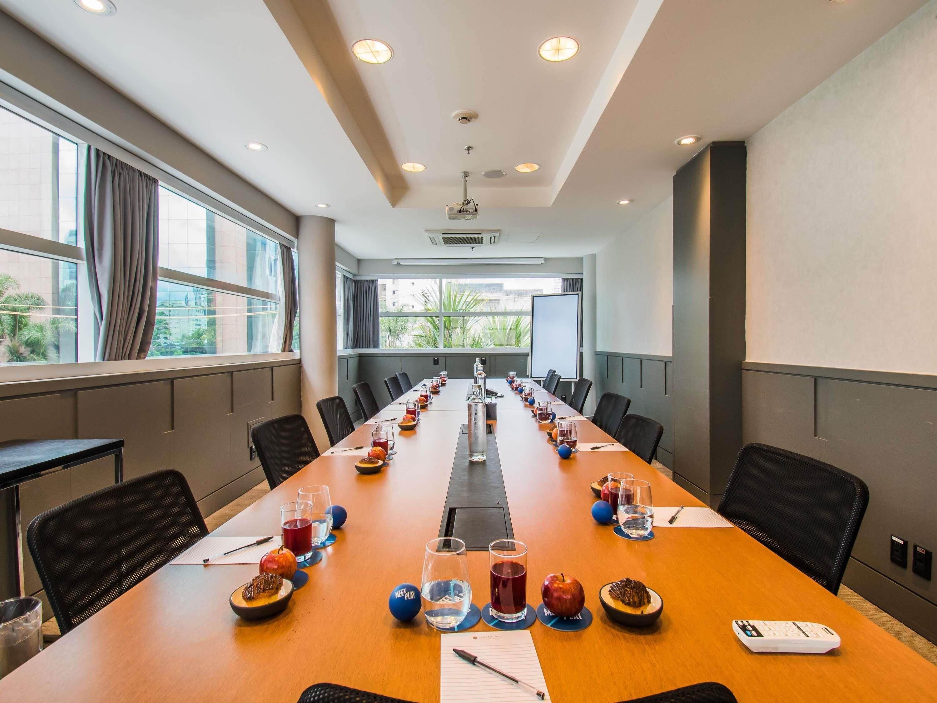 A conference room with a long table, chairs, and a projector screen.
