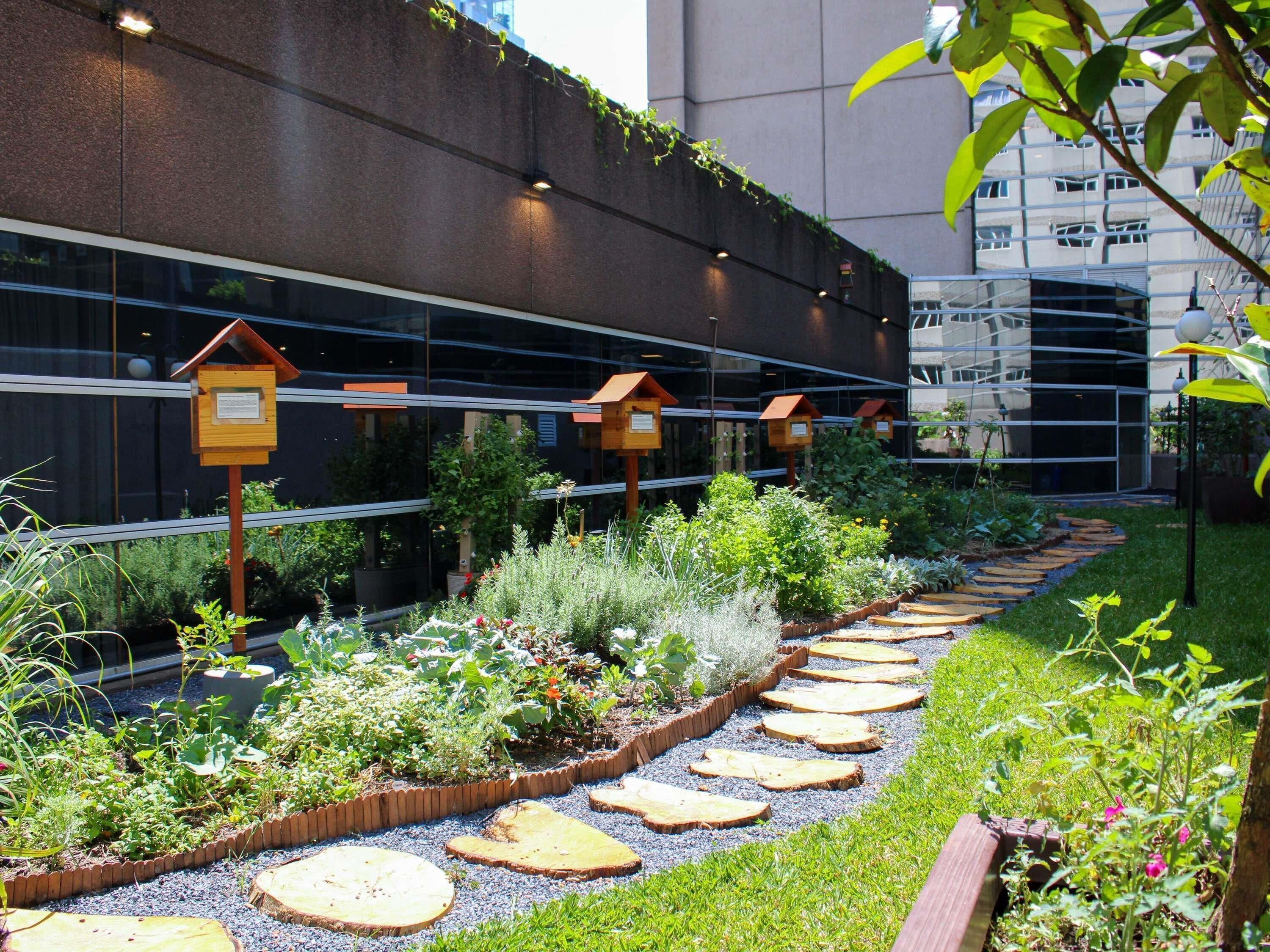 A garden pathway with wooden steps, surrounded by various plants and a building with reflective glass windows in the background.